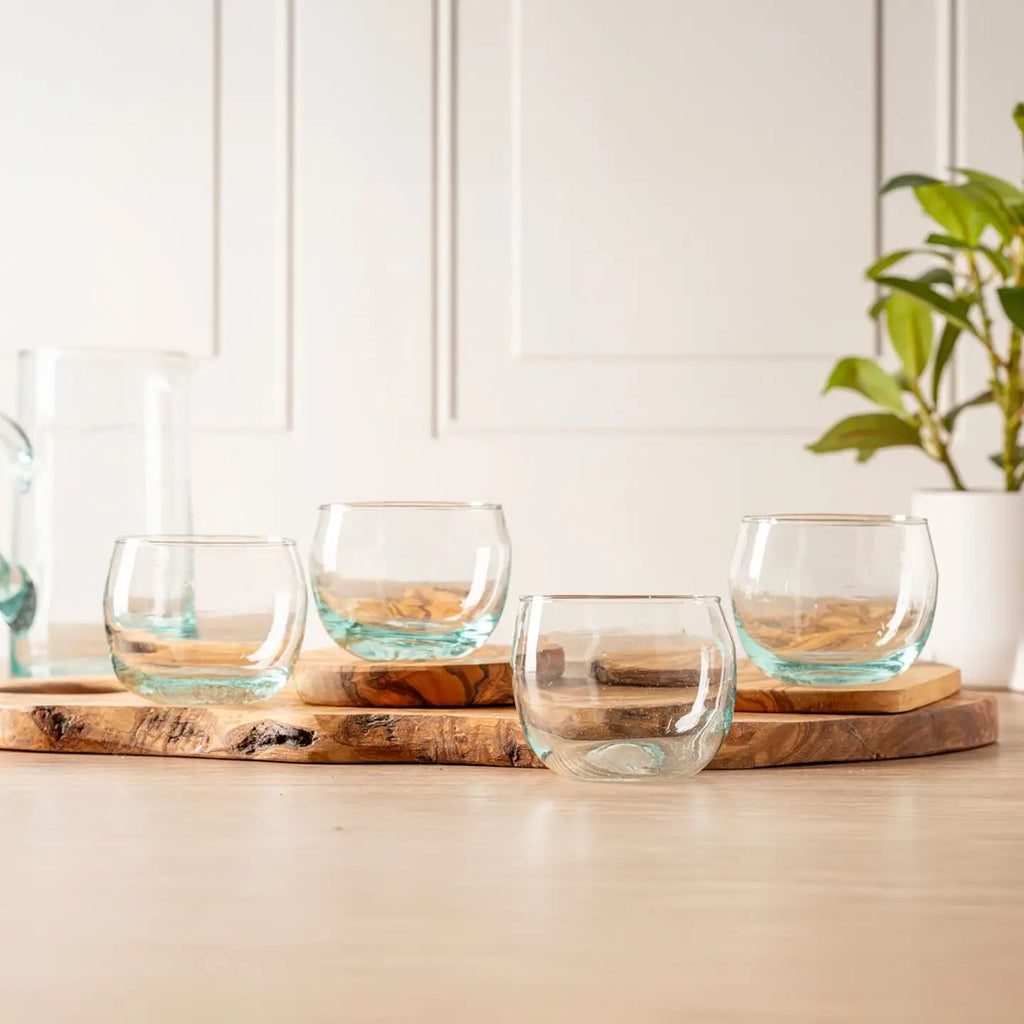 Set of clear glass tumblers on a wooden cutting board with a white wall and plant in the background