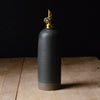 Black ceramic bottle with gold cap on a wooden surface