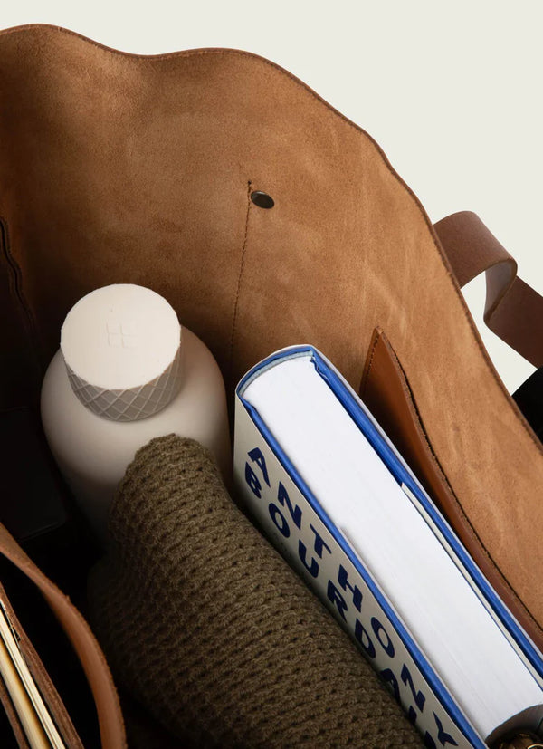 Brown leather bag with a bottle, book, and knitted item inside
