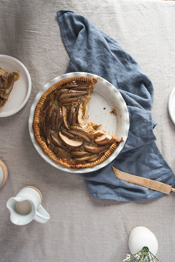 Pie with a slice missing on a table with a blue cloth and a knife.