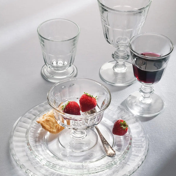 Clear glassware including a bowl with strawberries, a glass with red liquid, and a small glass on a white surface.