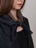 Person wearing a dark coat with a brown scarf tied around their neck against a plain background