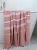 Pink towel with white stripes draped over a bathtub in a bathroom setting.