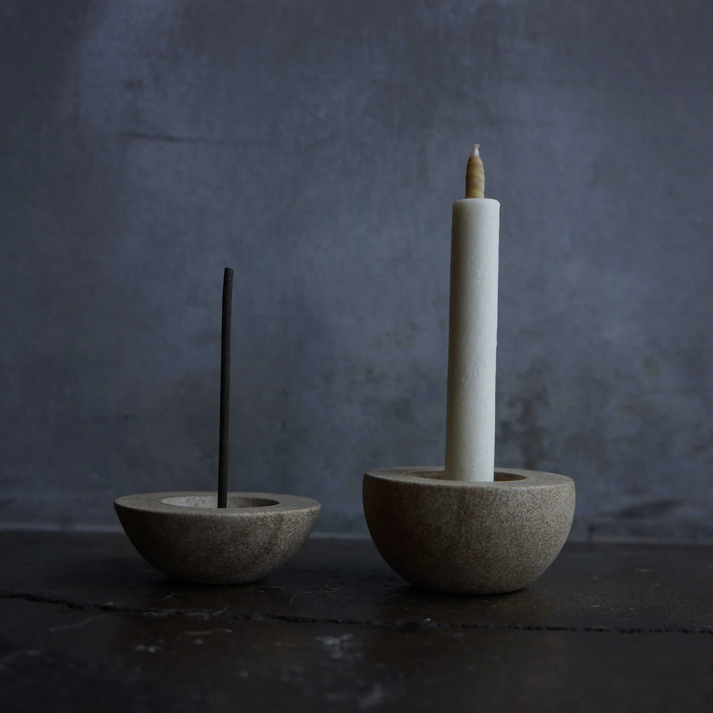 Two stone incense holders with a stick incense and a candle on a dark background
