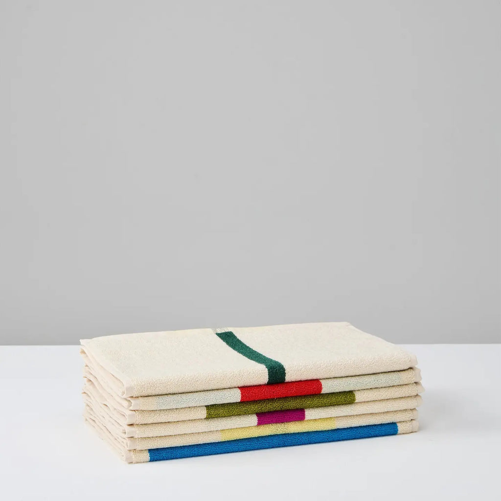 A stack of folded cream-colored woven towels with colorful stripes, including green, red, yellow, and blue, set against a minimalist light gray background.