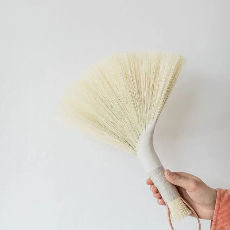 Hand holding a decorative broom against a plain background