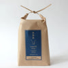 A kraft paper bag package tied with a thin ribbon at the top, featuring a blue front label with Japanese text and the English brand/product name Yamato Indigo.