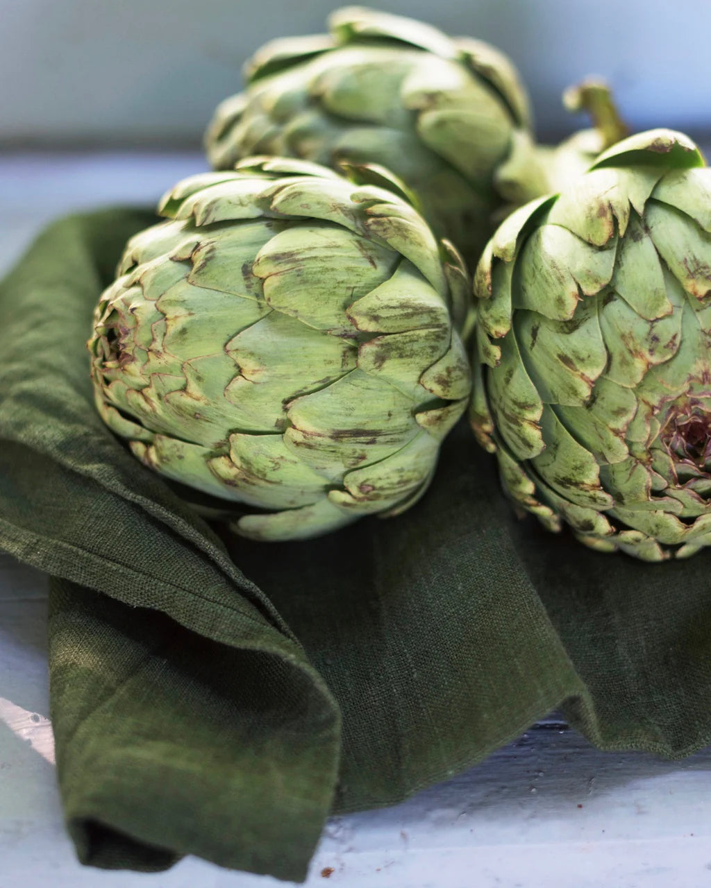 Three artichokes on a green cloth with a blurred background