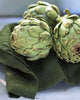 Three artichokes on a green cloth with a blurred background