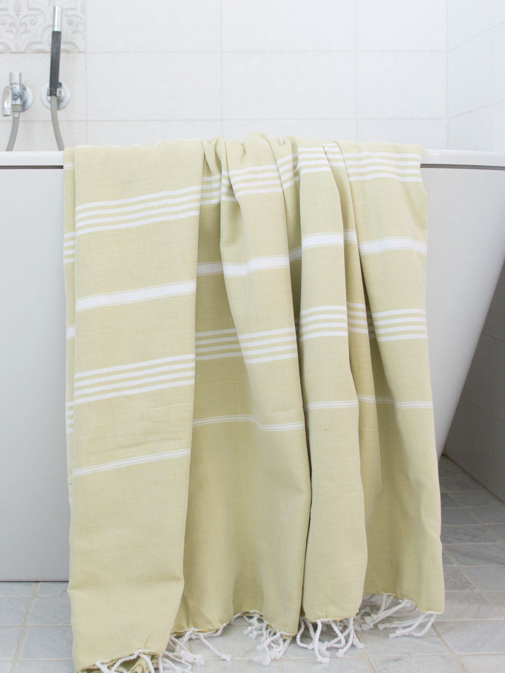 Yellow towel with white stripes draped over a bathtub in a bathroom setting.