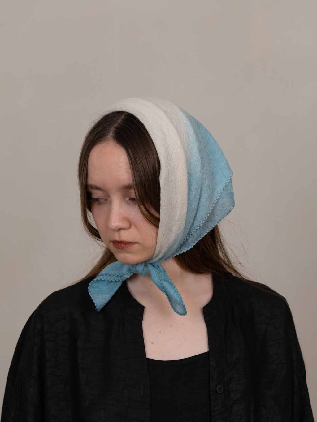 Woman wearing a light blue and white headscarf against a plain background