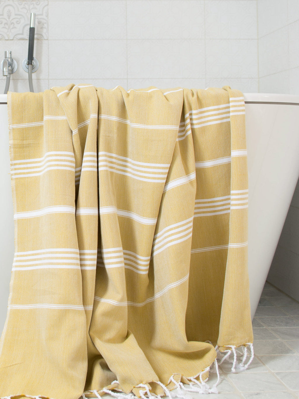 Yellow towel with white stripes draped over a bathtub in a bathroom setting.