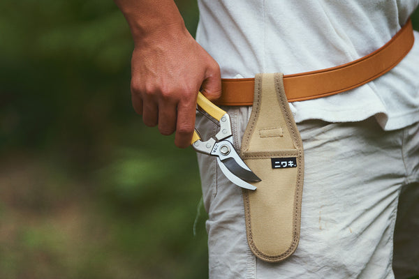 Person holding a pair of pruning shears in a leather sheath with a blurred natural background