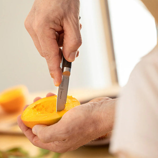 Person cutting a mango with a knife in a kitchen setting
