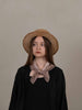 Woman wearing a straw hat and black outfit with a beige scarf against a plain background