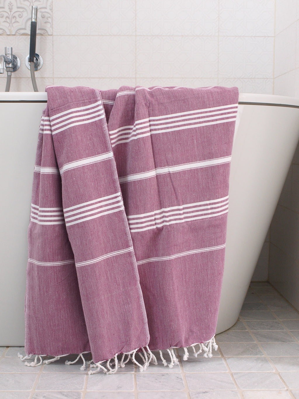 Purple towel with white stripes draped over a bathtub in a bathroom setting
