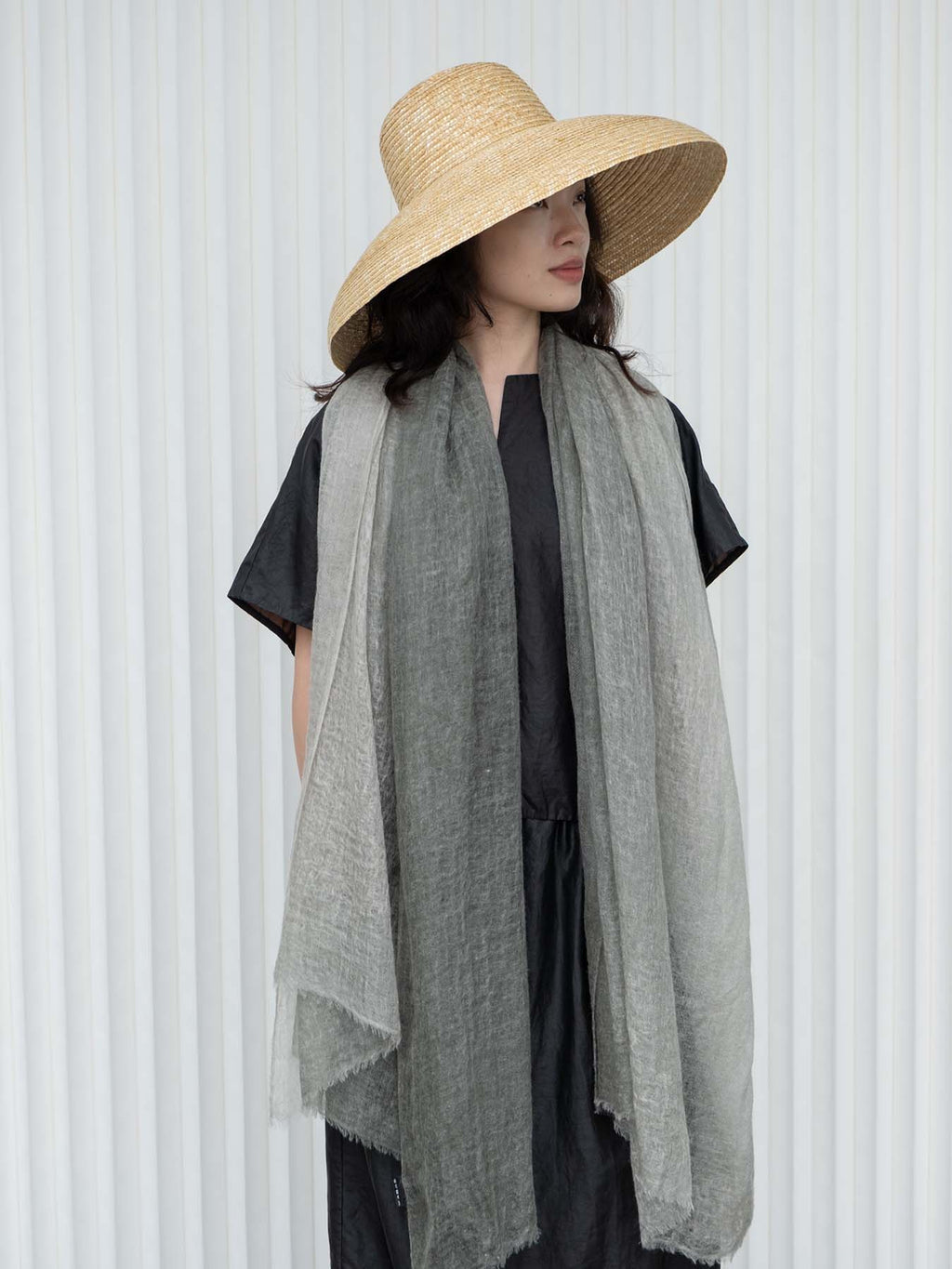 Woman wearing a wide-brimmed hat and gray scarf against a white background