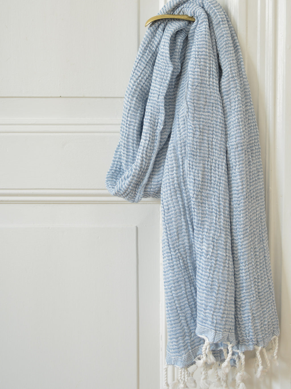 Blue and white checkered towel with tassels hanging on a white door.