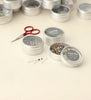 Silver tins with pins and a red scissors on a light background
