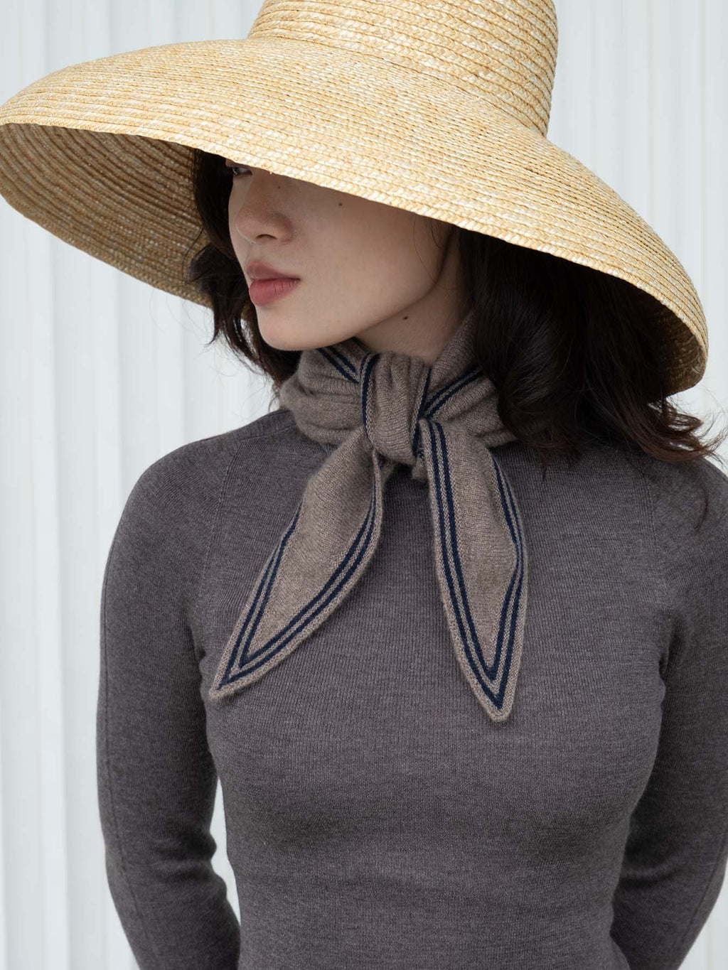 Woman wearing a wide-brimmed hat and a gray sweater with a scarf.