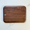 A rectangular wooden cutting board with rounded corners and a small circular hole on the left side, shown on a white marble surface.