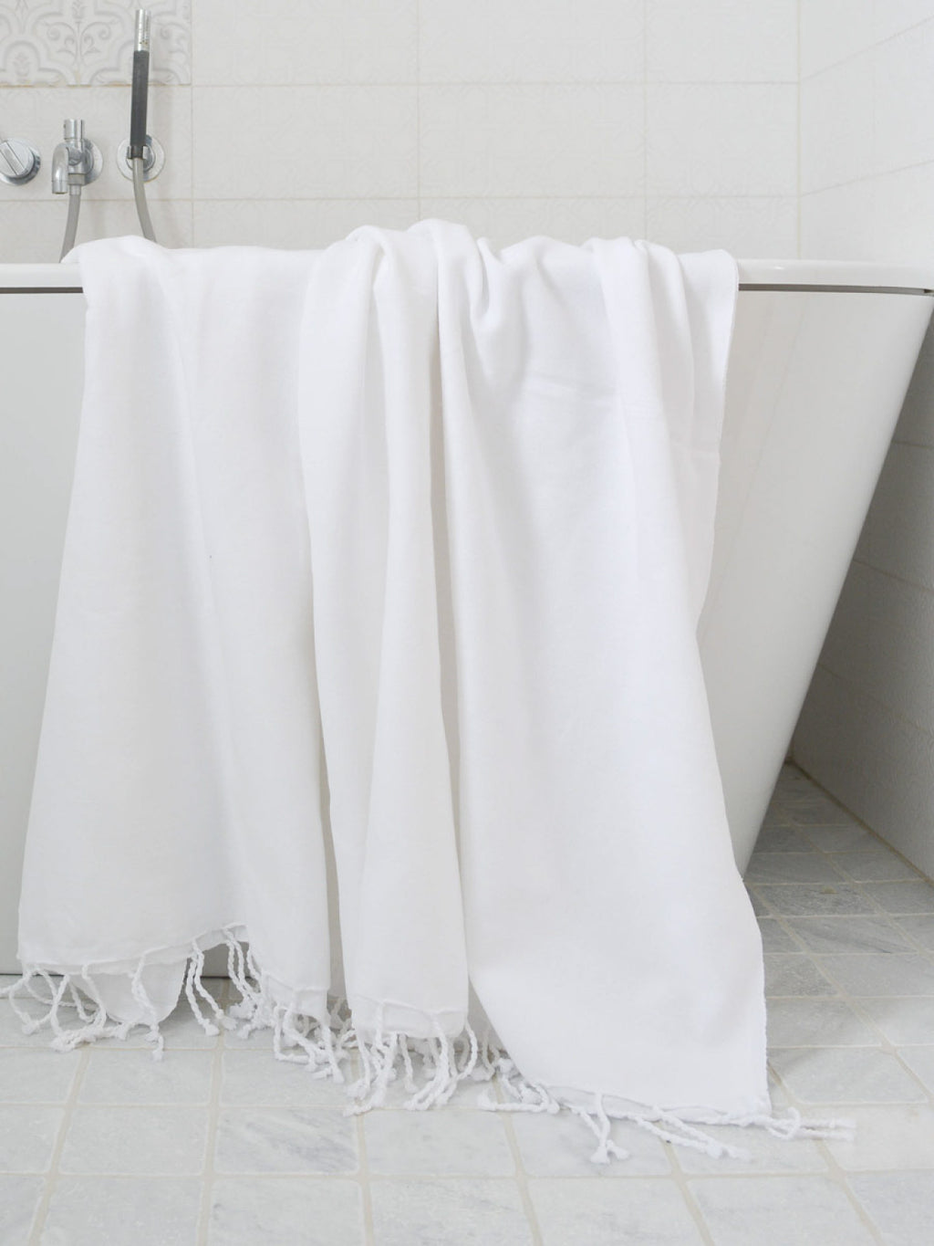 White towel with fringes draped over a bathtub in a bathroom setting.