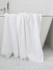 White towel with fringes draped over a bathtub in a bathroom setting.