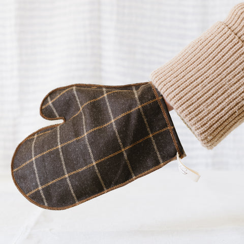 A two-tone checkered polishing mitt, with a beige and dark checkered pattern, held up against a blurred background.