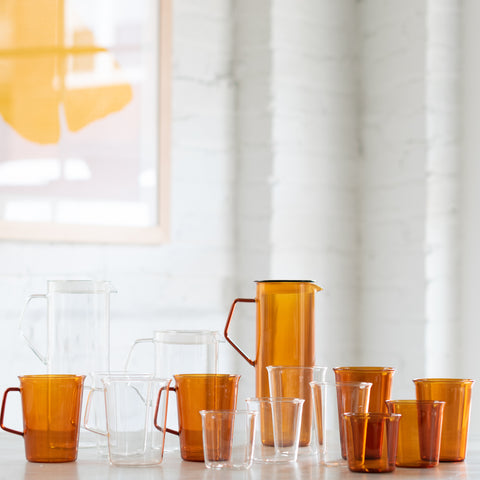 A selection of amber and clear glassware from the CAST collection, including various sizes of cups, glasses, and jugs, displayed on a table.